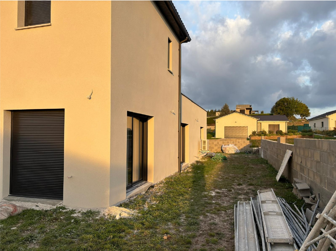 Vue latérale d'une maison beige clair avec une porte de garage noire et une cour étroite.