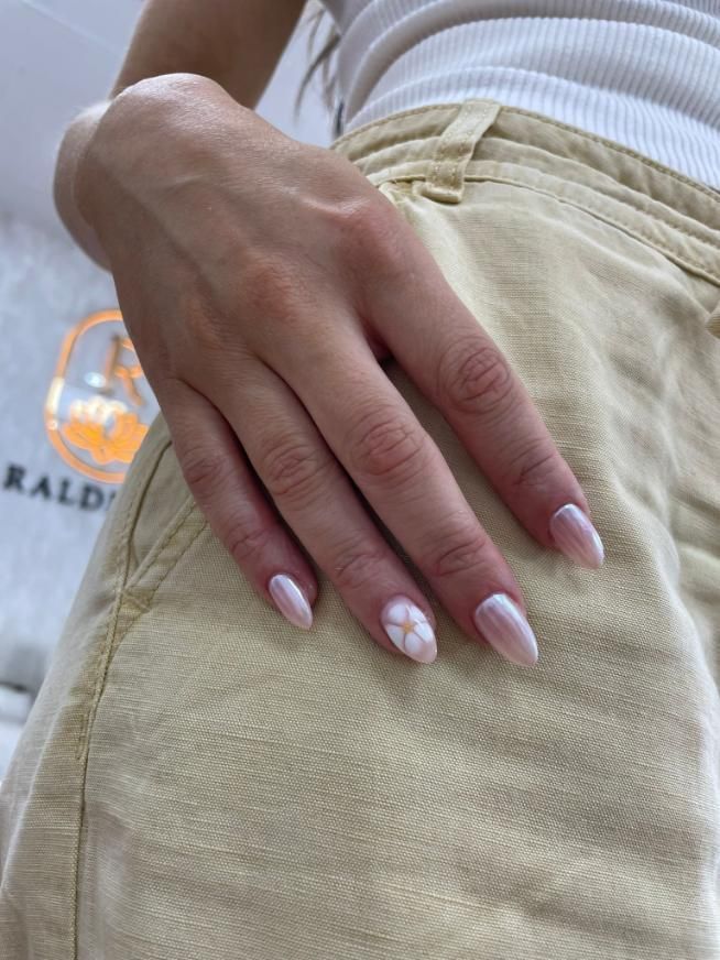 Mano con uñas de forma ovalada, manicura francesa y diseño floral, apoyada sobre un pantalón color canela.