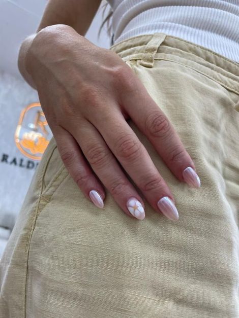 Mano con uñas de forma ovalada, manicura francesa y diseño floral, apoyada sobre un pantalón color canela.