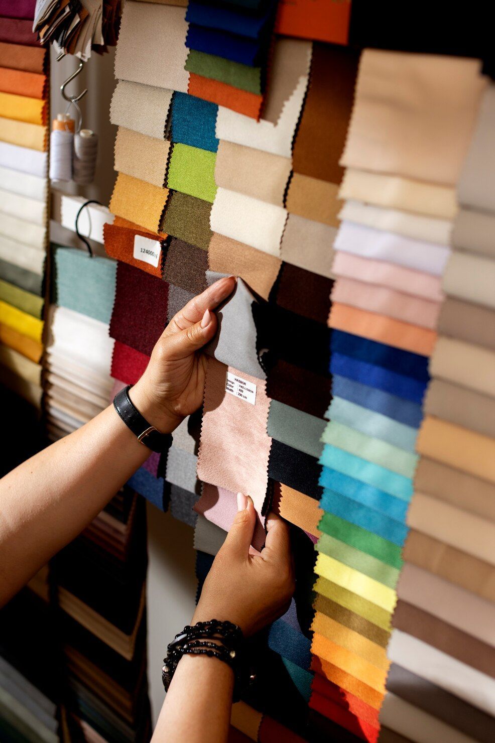 Manos sosteniendo una muestra de tela frente a una pared de coloridas muestras textiles.