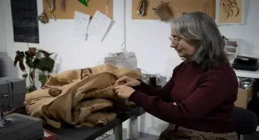 Una mujer está sentada en una mesa trabajando en un trozo de tela.