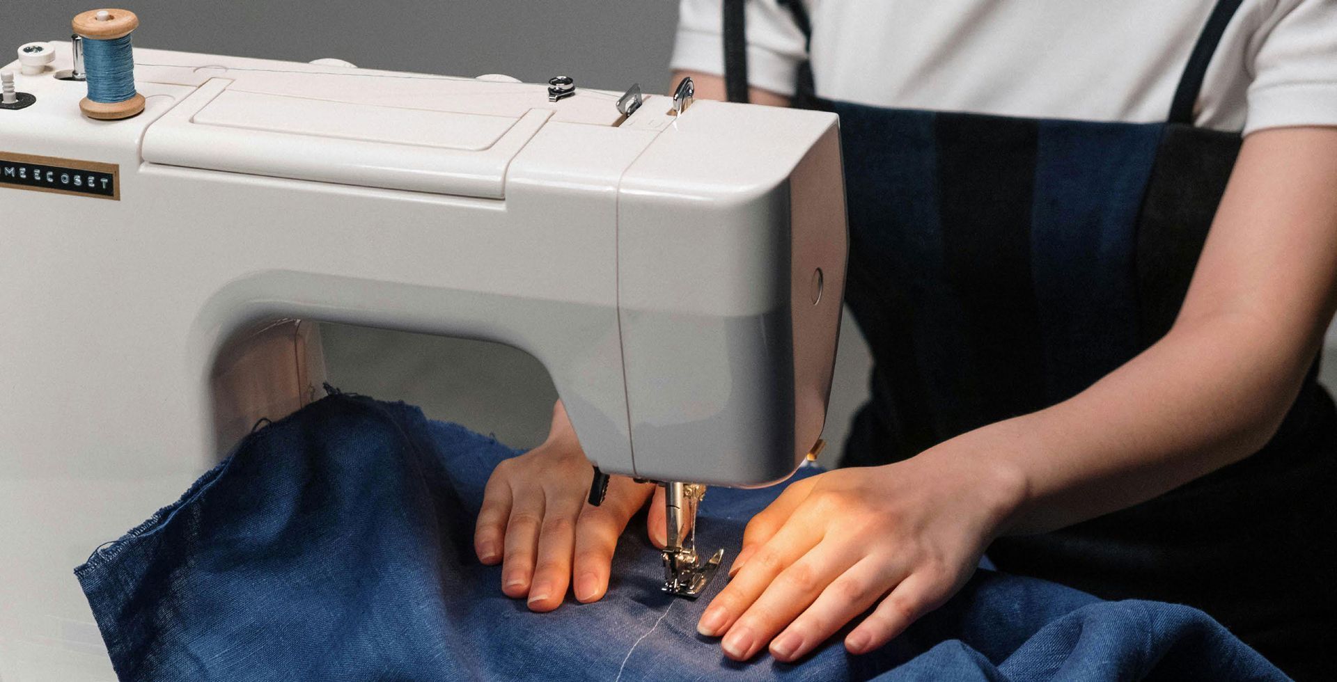 Una mujer está usando una máquina de coser para coser un trozo de tela azul.