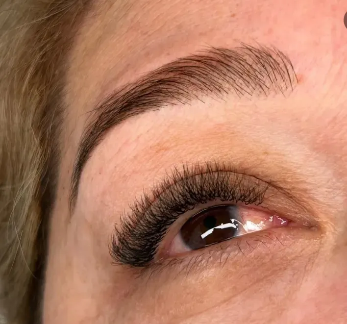 Primer plano de un ojo con largas extensiones de pestañas oscuras y una ceja bien definida.