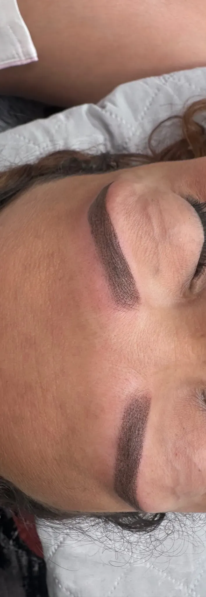 Primer plano del ojo cerrado de una persona, con una ceja oscura y delineador de ojos, recostada de lado.