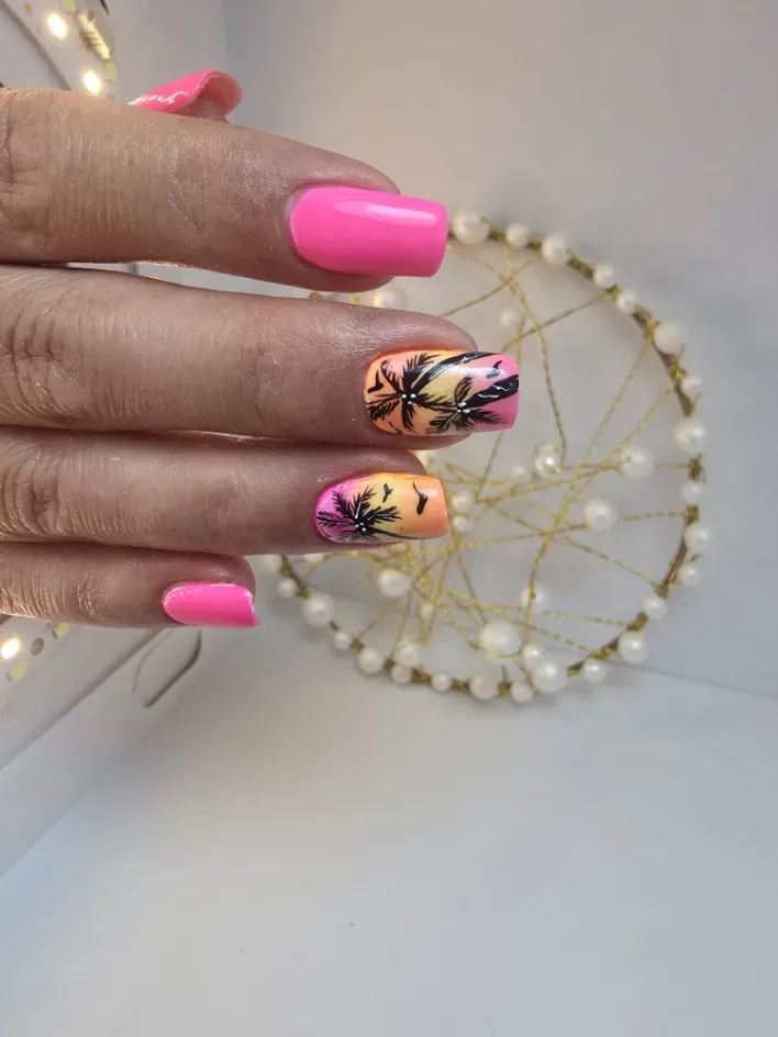 Mano con uñas de color rosa brillante y un diseño floral junto a un adorno de atrapasueños de perlas.