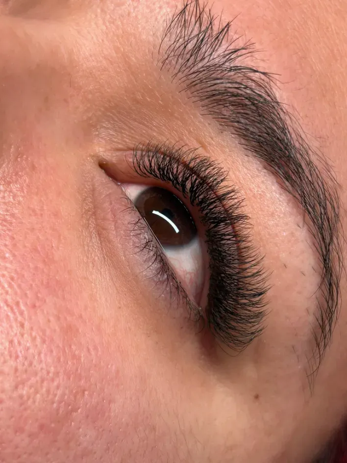 Primer plano del ojo de una persona con pestañas largas y una ceja oscura, visto desde un ángulo.