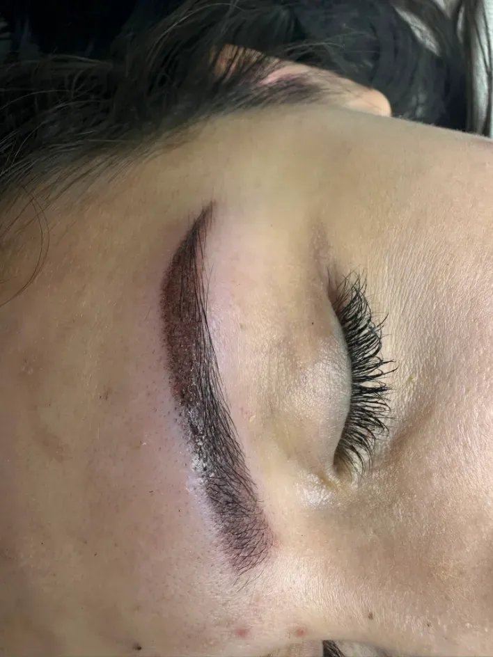 Primer plano de un ojo cerrado con ceja oscura y pestañas rizadas sobre piel clara.