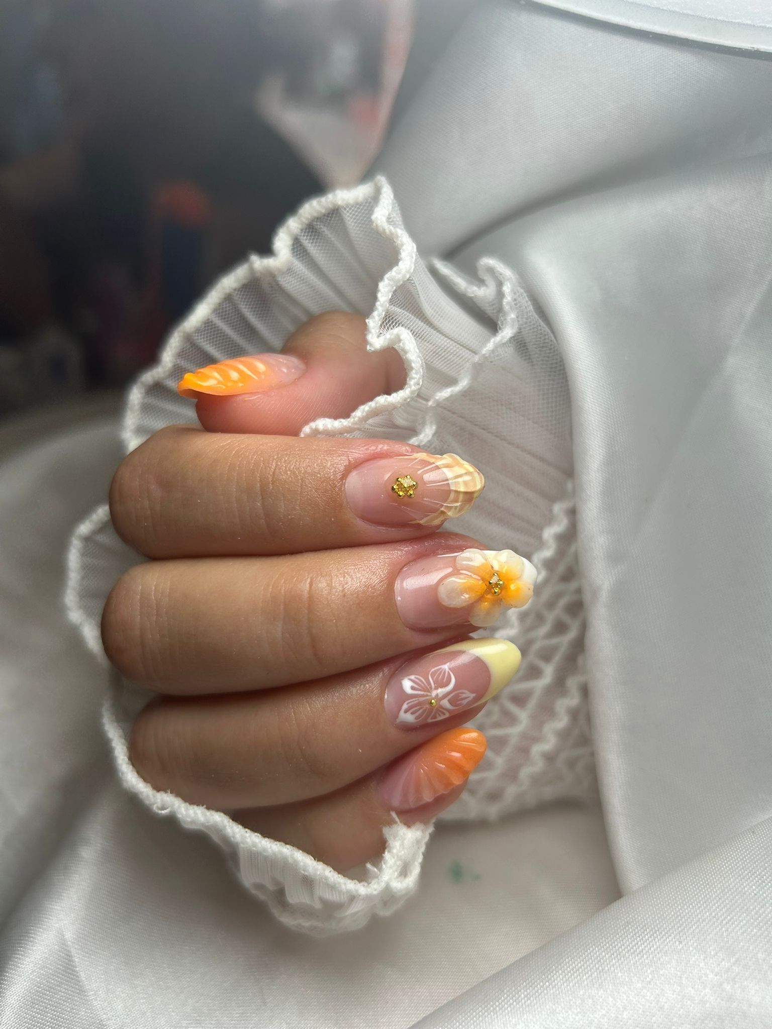 Mano con manicura floral rosa descansando sobre una superficie blanca junto a un plato decorativo con cuentas doradas.