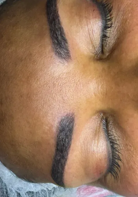 Primer plano de ojos cerrados con cejas oscuras bien definidas y sombra de ojos dorada brillante.