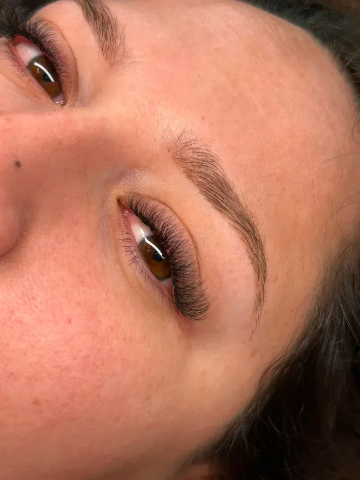 Primer plano de un rostro con ojos marrones, cejas bien definidas y pestañas largas sobre un fondo cálido.