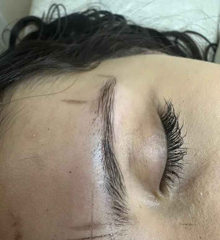 Primer plano de un ojo cerrado con pestañas largas y una ceja bien definida sobre un fondo claro.