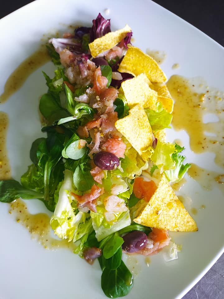 Ensalada con verduras mixtas, salmón, aceitunas y chips de tortilla en un plato blanco, rociada con aderezo.