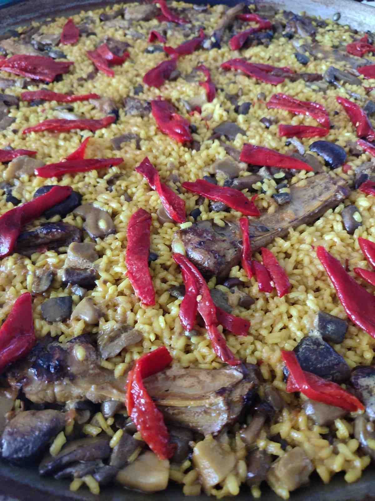 Paella con arroz amarillo, champiñones y tiras de pimiento rojo en una sartén grande.