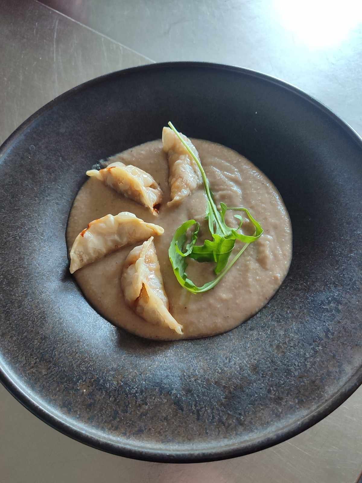 Un plato de comida: empanadillas sobre sopa cremosa, con guarnición de hojas verdes.