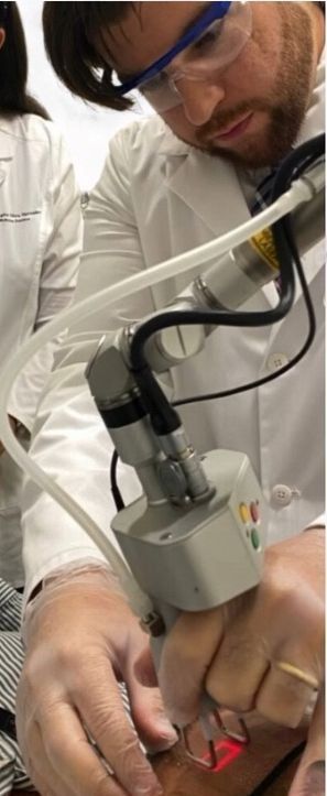 Un hombre con una bata de laboratorio está usando una máquina para eliminar un tatuaje.