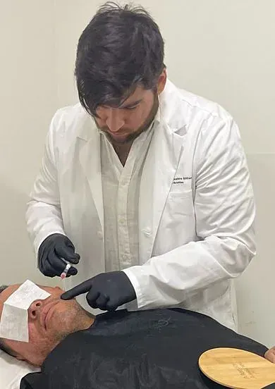 Un hombre con una bata blanca y guantes negros le está dando a un hombre un tratamiento facial.