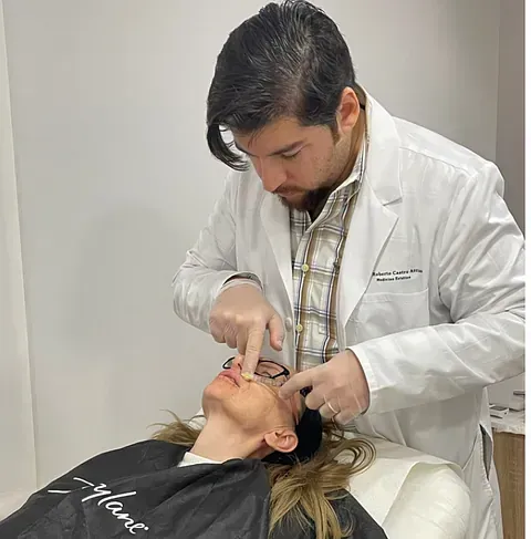 Un hombre con una bata blanca examina el rostro de una mujer.