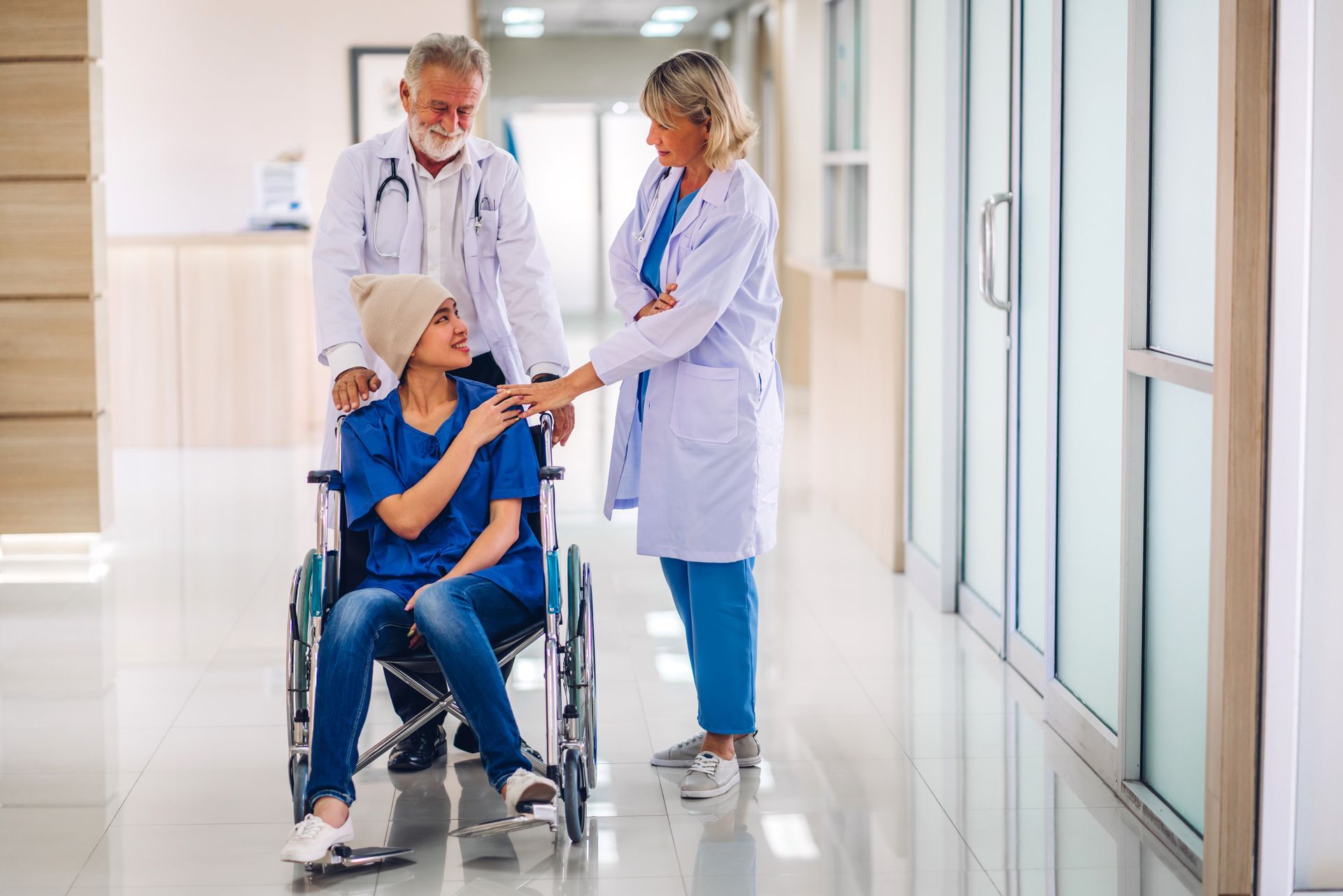 ein Patient im Rollstuhl wird von zwei Ärzten begleitet