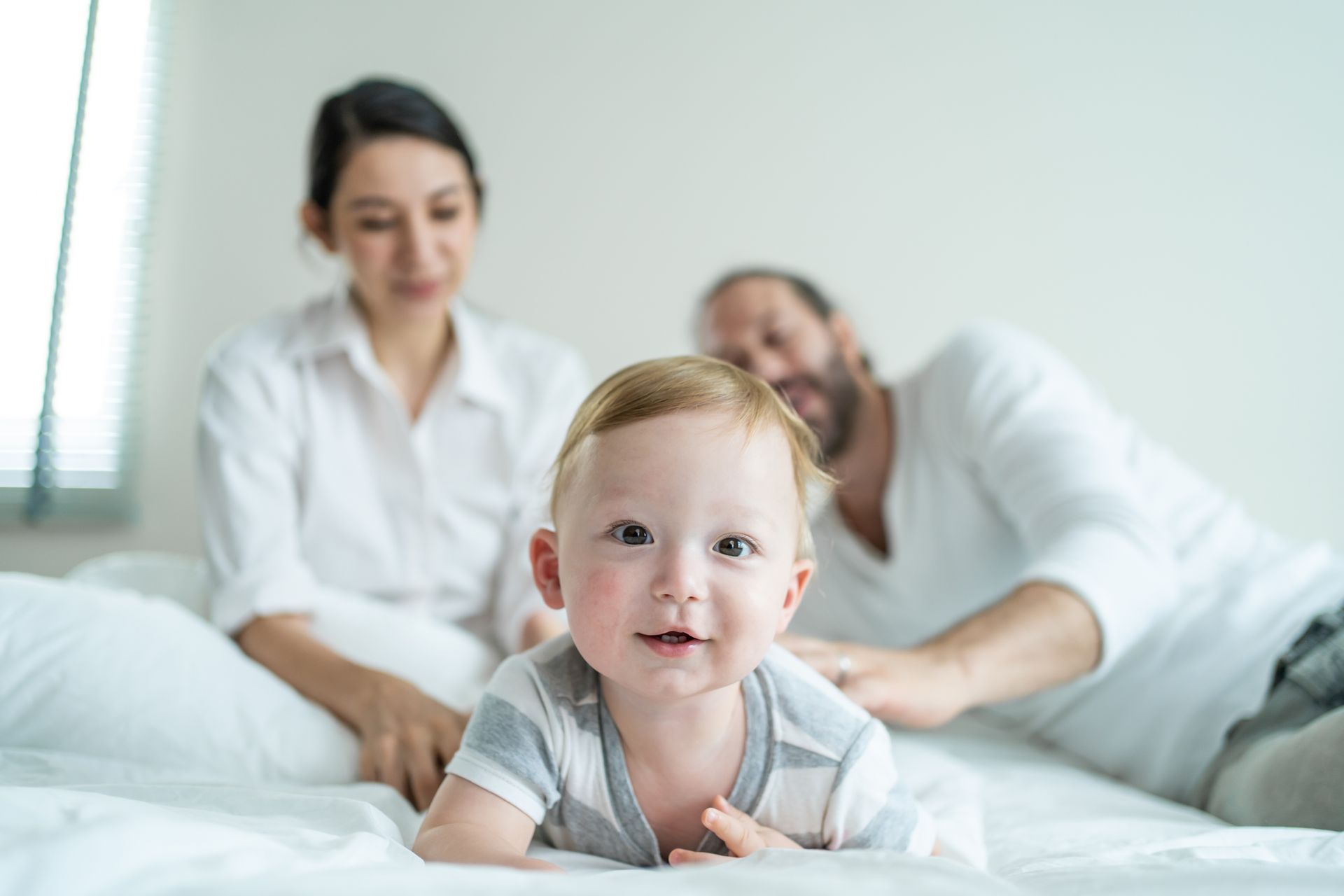 ein Baby liegt auf einem Bett mit einem Mann und einer Frau im Hintergrund