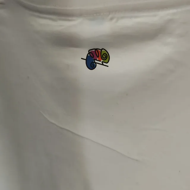 Un camaleón está bordado en la espalda de una camisa blanca.