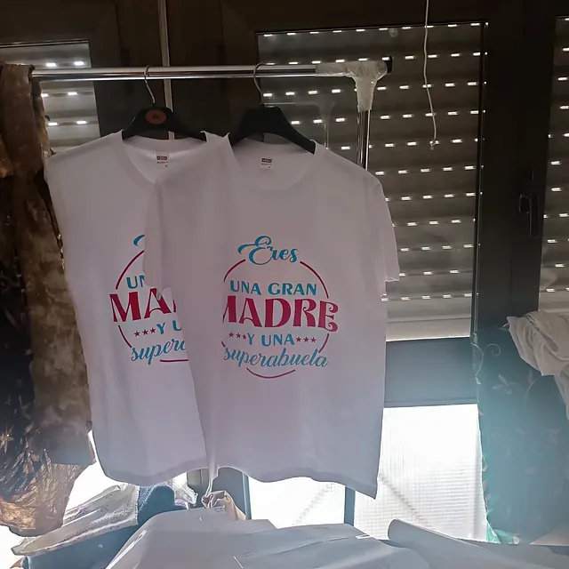 Dos camisetas están colgadas en un perchero delante de una ventana.