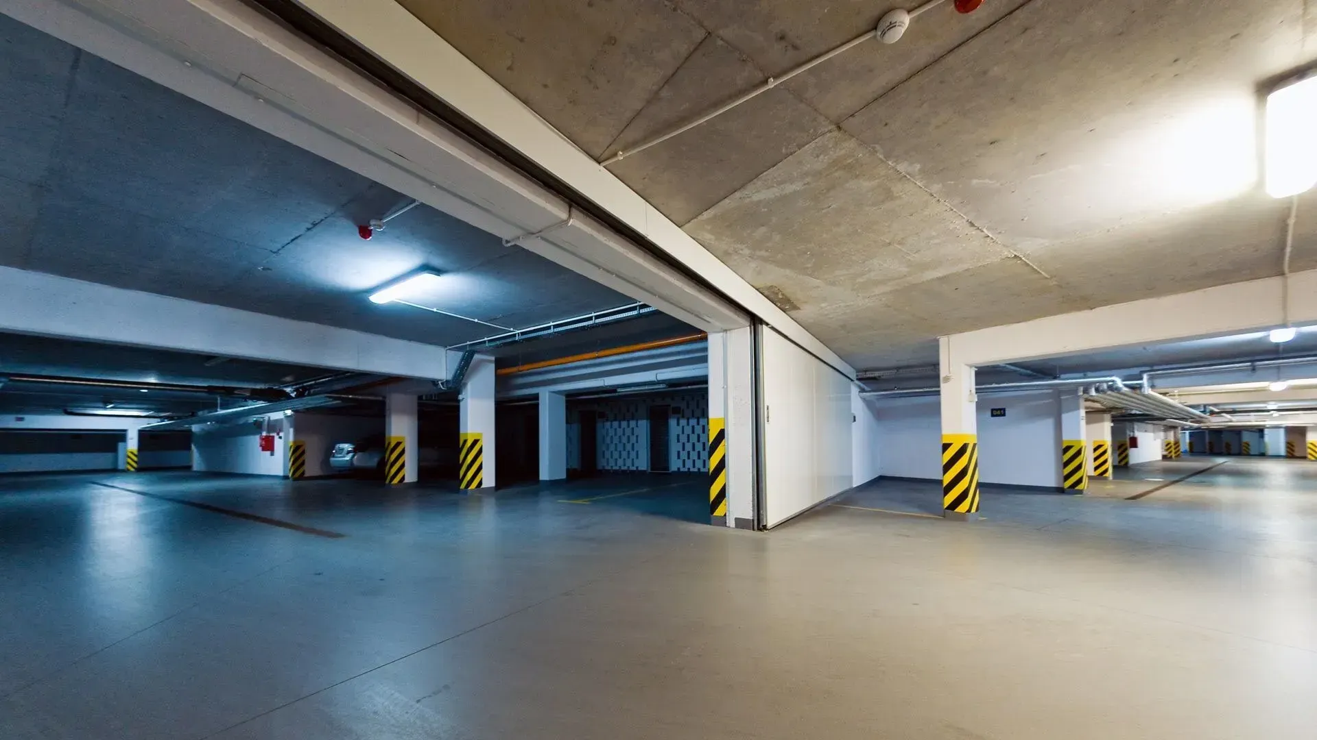 Garagem de estacionamento vazia e bem iluminada, com colunas de sustentação e teto de concreto.