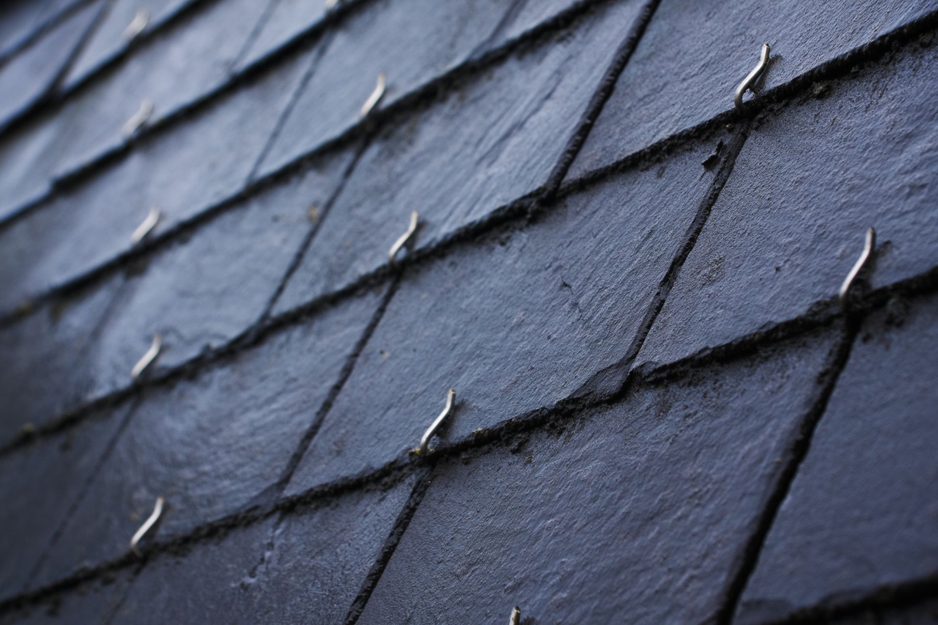 Tuiles de toit en ardoise gris foncé avec fixations métalliques.