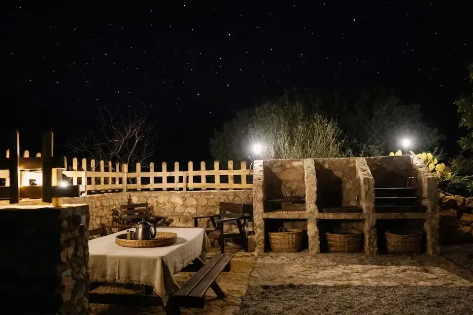 Comedor nocturno al aire libre con mesas, bancos de madera y luces cálidas bajo un cielo estrellado.