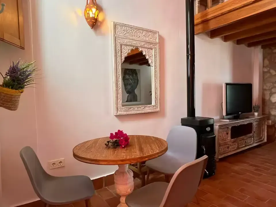 Acogedor rincón comedor con mesa redonda de madera, sillas grises, espejo de pared y televisor