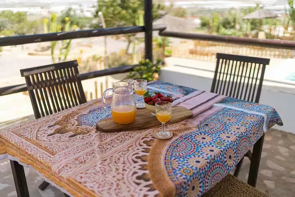 Conjunto de mesa y sillas de patio al aire libre con zumo de naranja, fruta y pan con vistas al jardín.