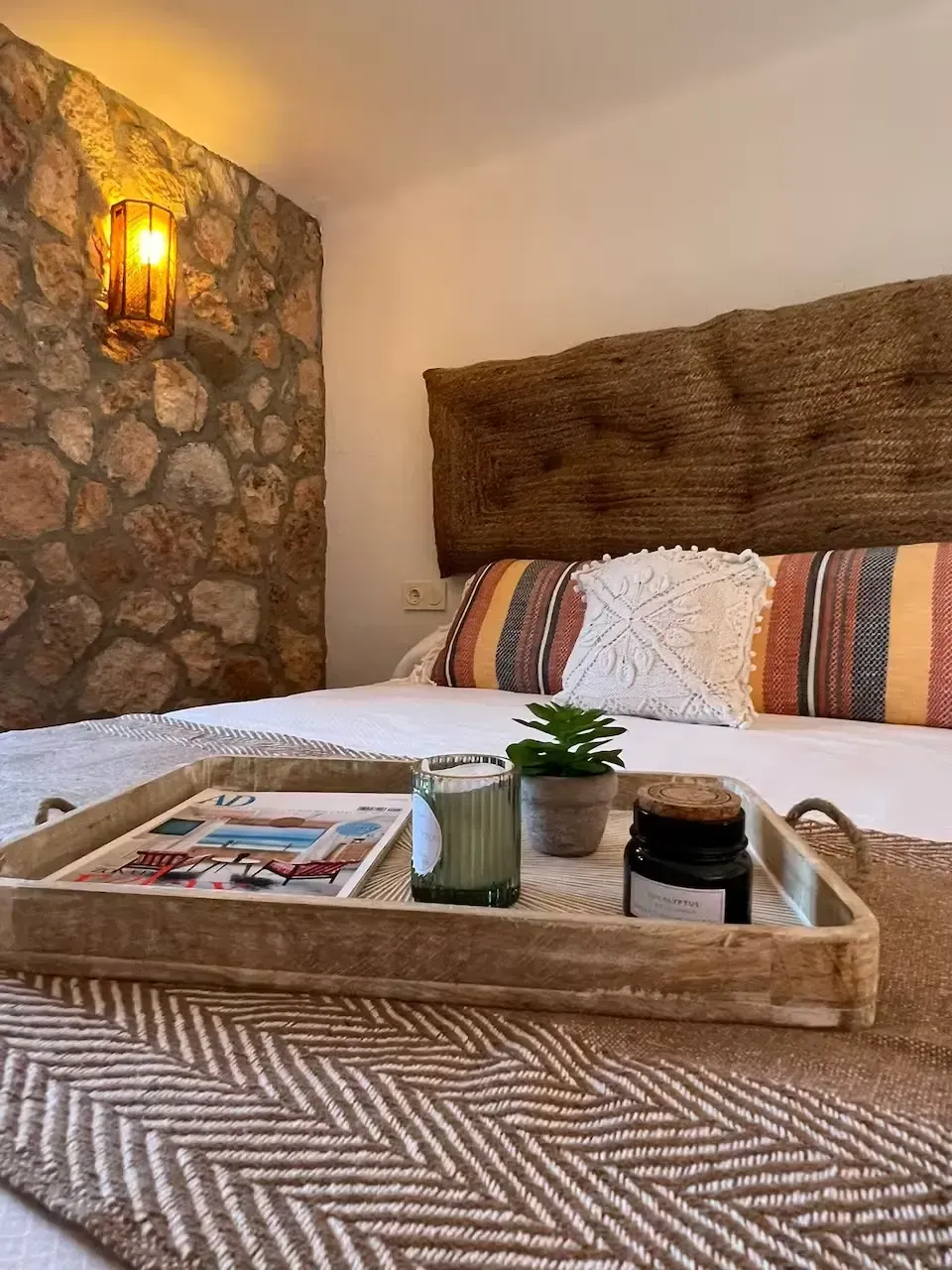 Acogedor dormitorio con pared decorativa de piedra, cabecero tejido, bandeja sobre la cama