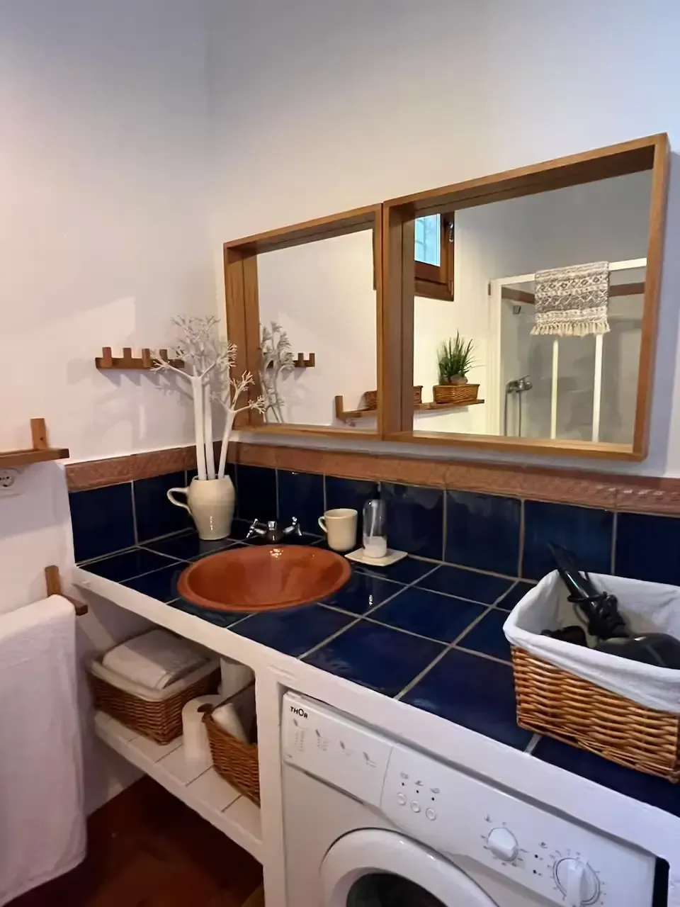 Mueble de baño con lavabo de cobre, encimera de azulejos azules, espejo con marco de madera