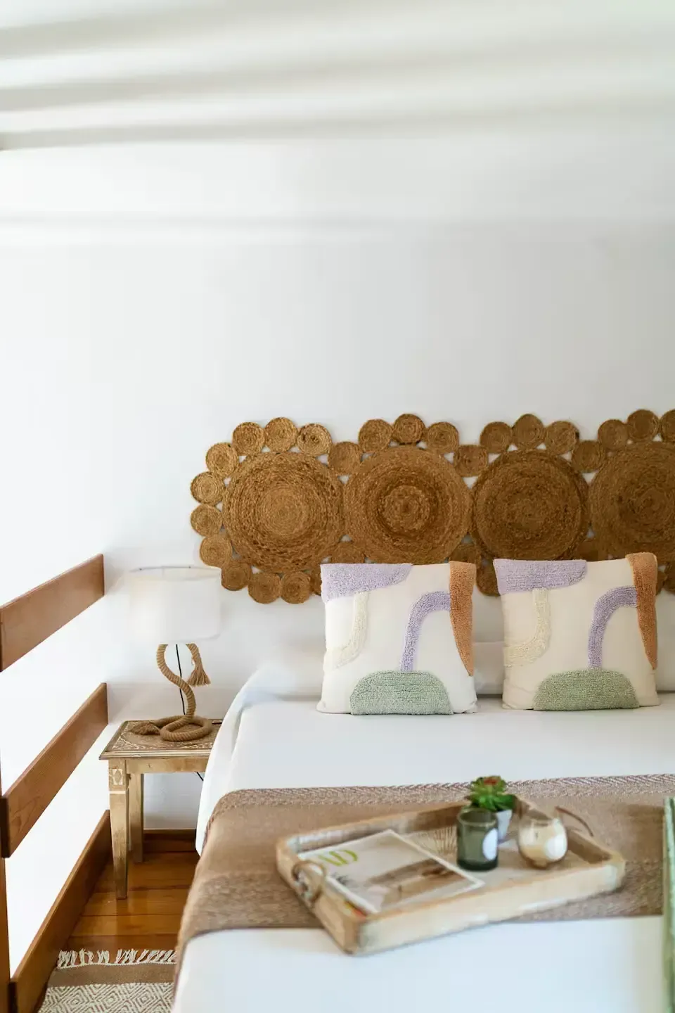 Habitación acogedora con cabecero de madera tallada, dos almohadas estampadas y una bandeja sobre una cama bien hecha.