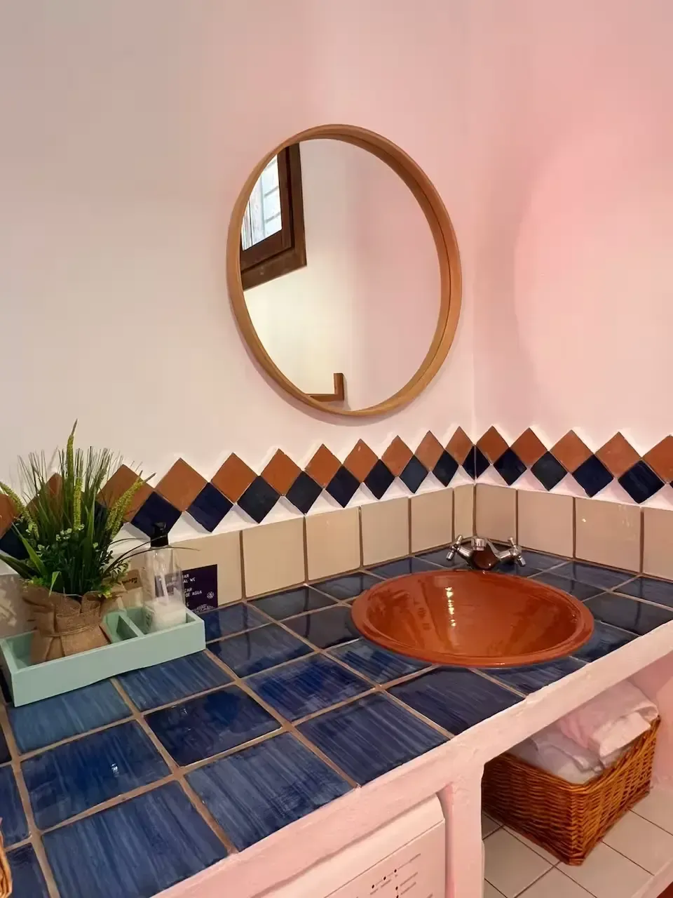 Tocador de baño con azulejos azules, lavabo de cobre, espejo redondo y protector contra salpicaduras con diseño.