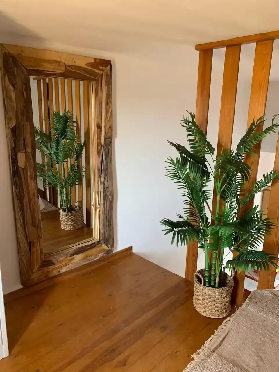 Rincón de la sala de estar con un gran espejo con marco de madera, una planta en maceta y un sofá color canela