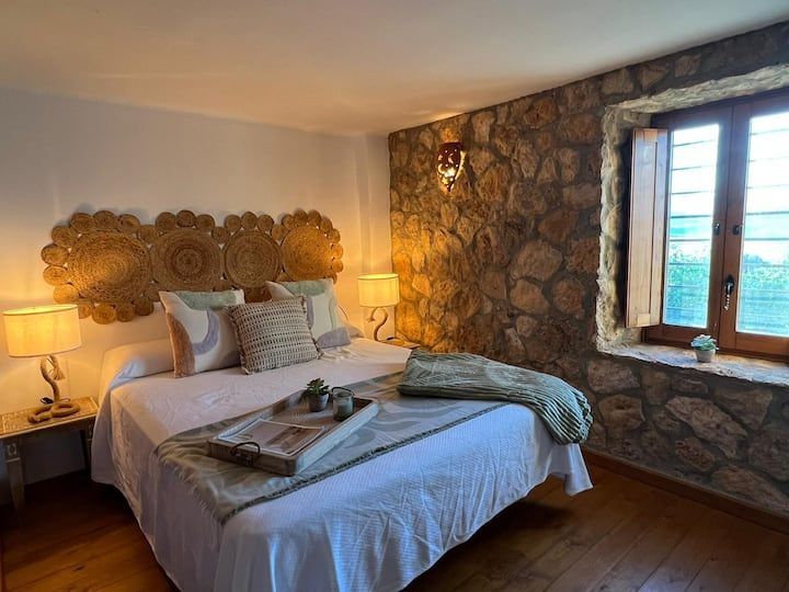 Un dormitorio con una cama, lámparas, una ventana y una pared de piedra.
