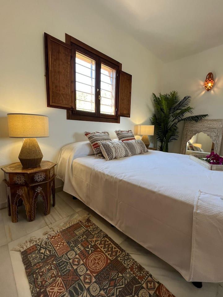 Un dormitorio con una cama, lámparas, una alfombra y una ventana.