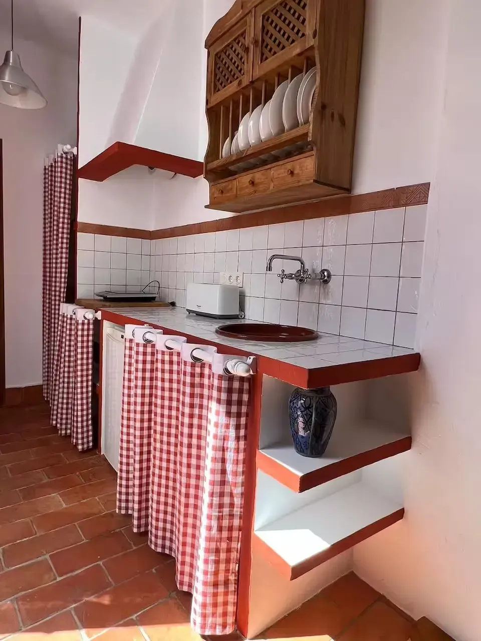 Encimera de cocina rústica con cortinas a cuadros rojos y blancos, salpicadero de azulejos blancos