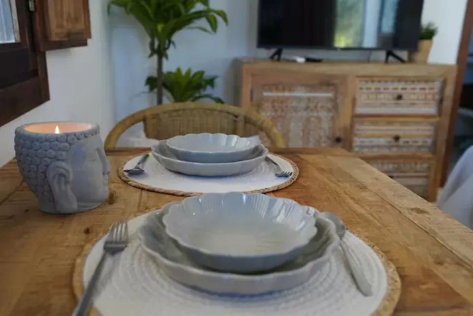Prepara la mesa del comedor con platos blancos y una vela gris sobre una mesa de madera en una acogedora sala de estar.