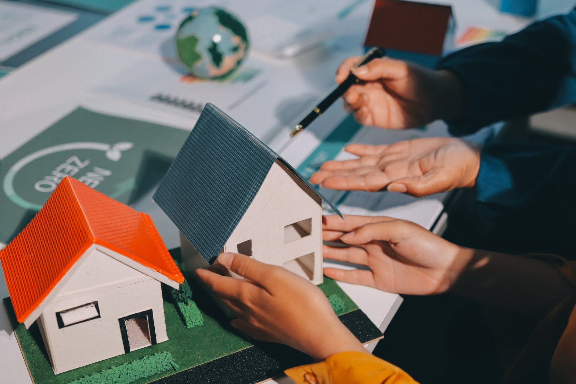 Una persona le entrega la llave de una casa a otra persona sobre un escritorio donde hay una pequeña maqueta de la casa y un contrato.