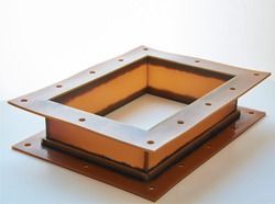 Una pieza rectangular de metal con agujeros reposa sobre una superficie blanca.