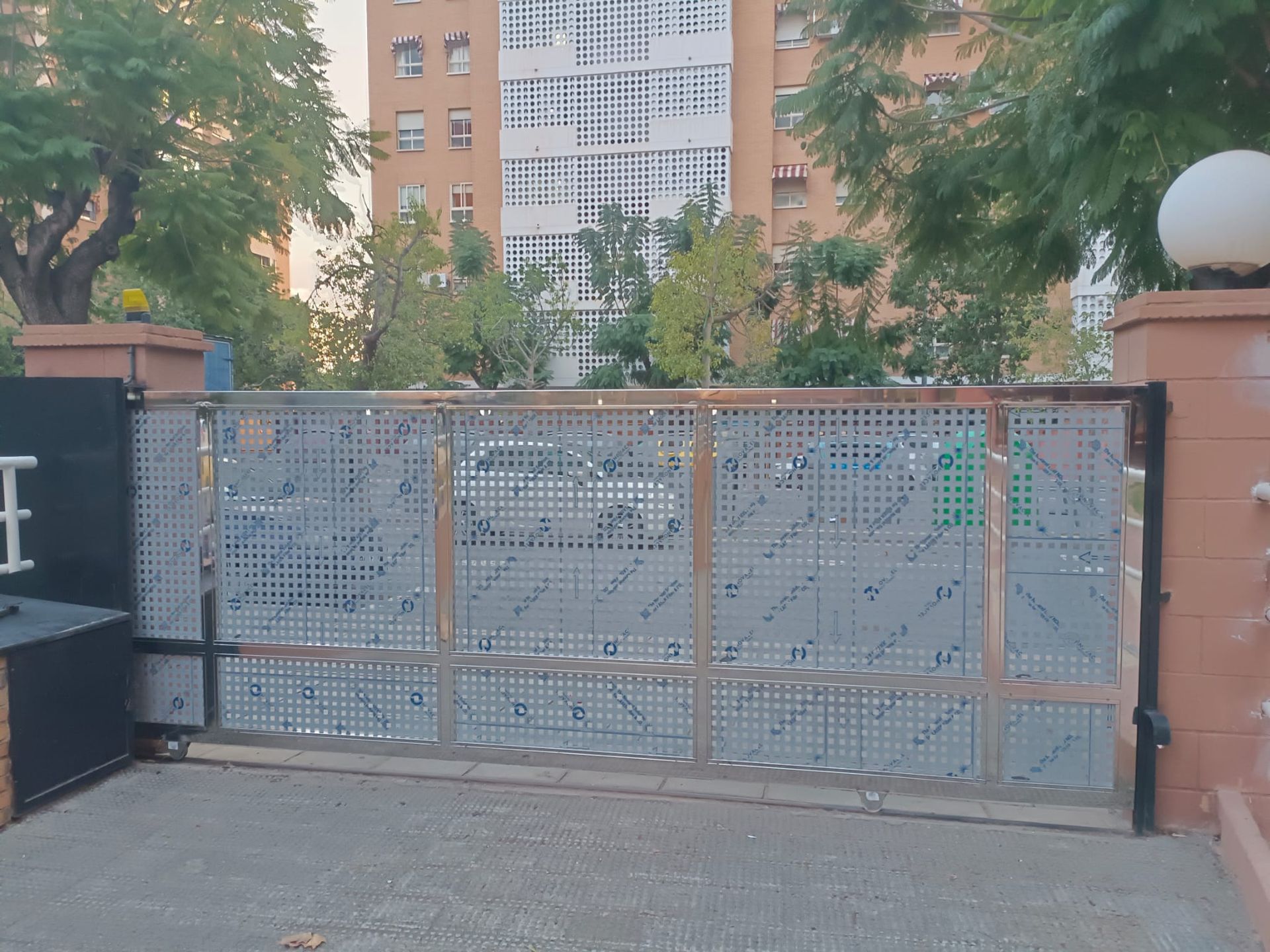 Portón metálico con diseño estampado, parcialmente abierto, frente a un edificio de departamentos.