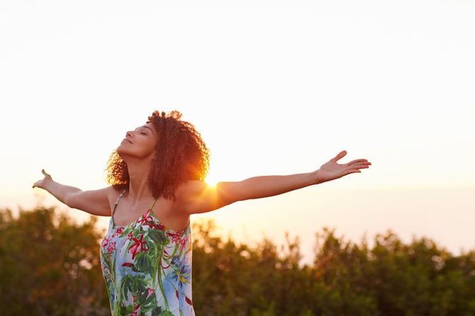 Una mujer está parada en un campo con los brazos extendidos al atardecer.