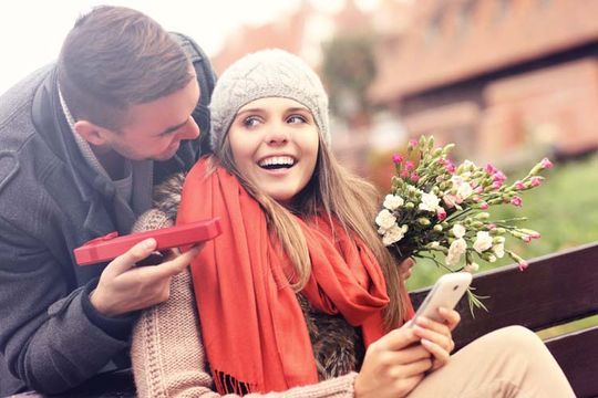 Un hombre le da a una mujer un ramo de flores y un regalo.