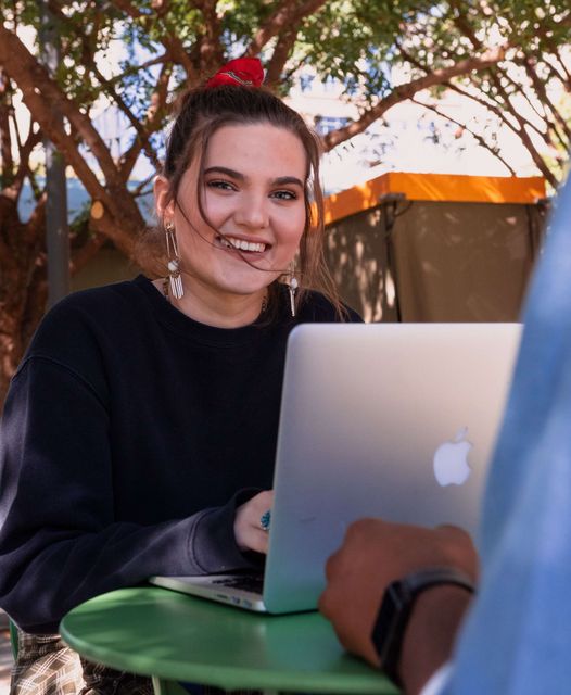 Eine Frau lächelt, während sie einen Apple-Laptop benutzt