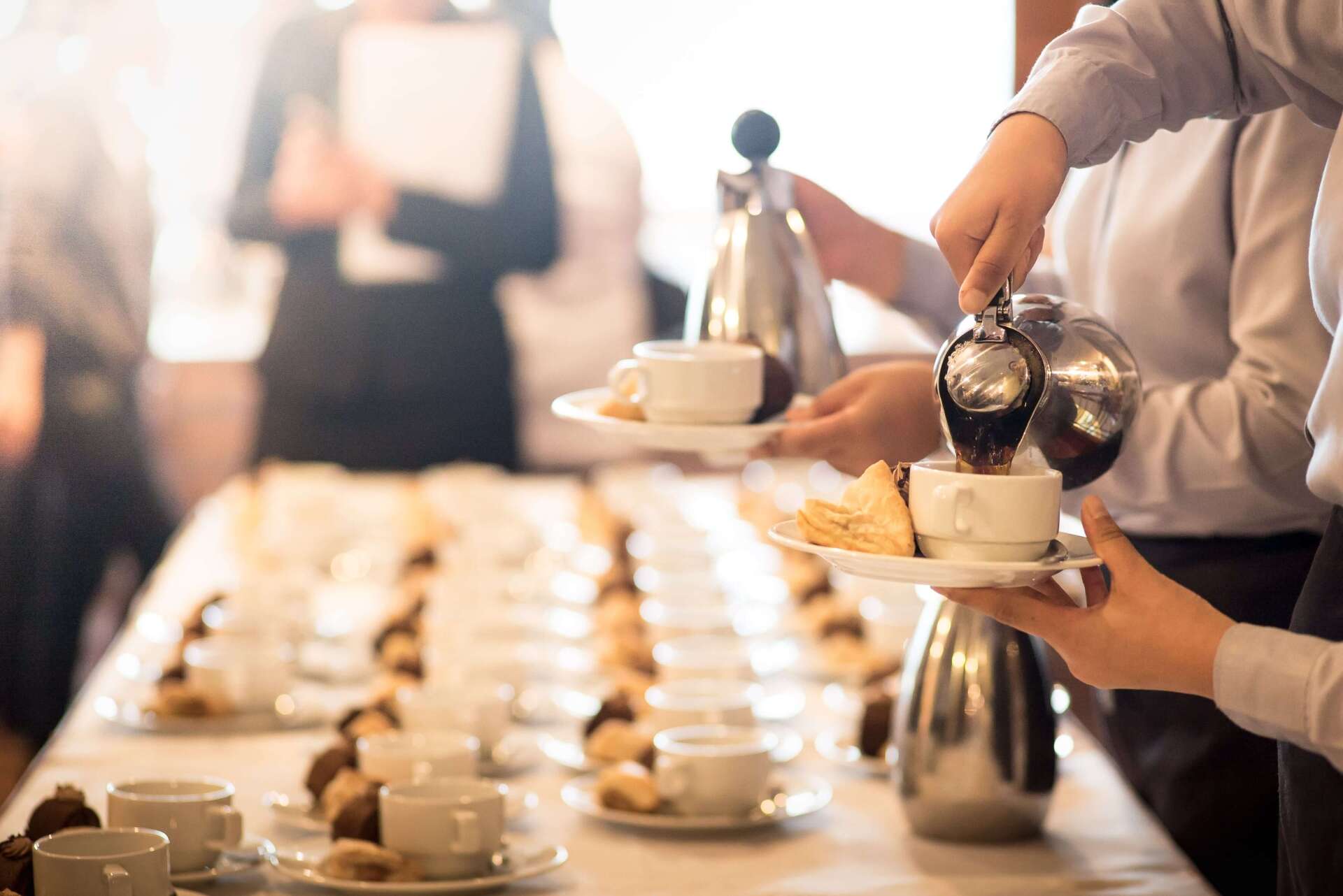 Eine Gruppe von Menschen gießt Kaffee in Tassen auf einem Tisch.