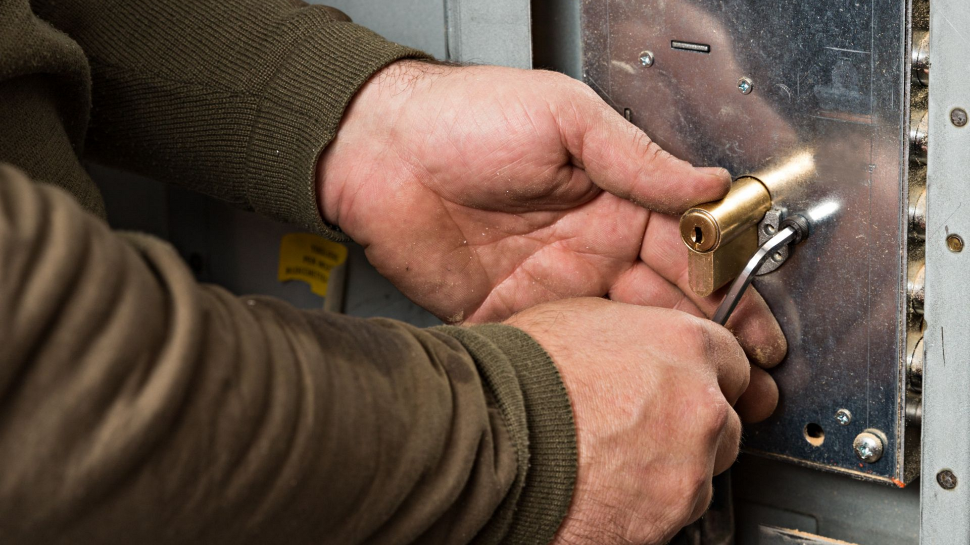 Des mains manipulent un outil sur un mécanisme de serrure ; à l'intérieur.