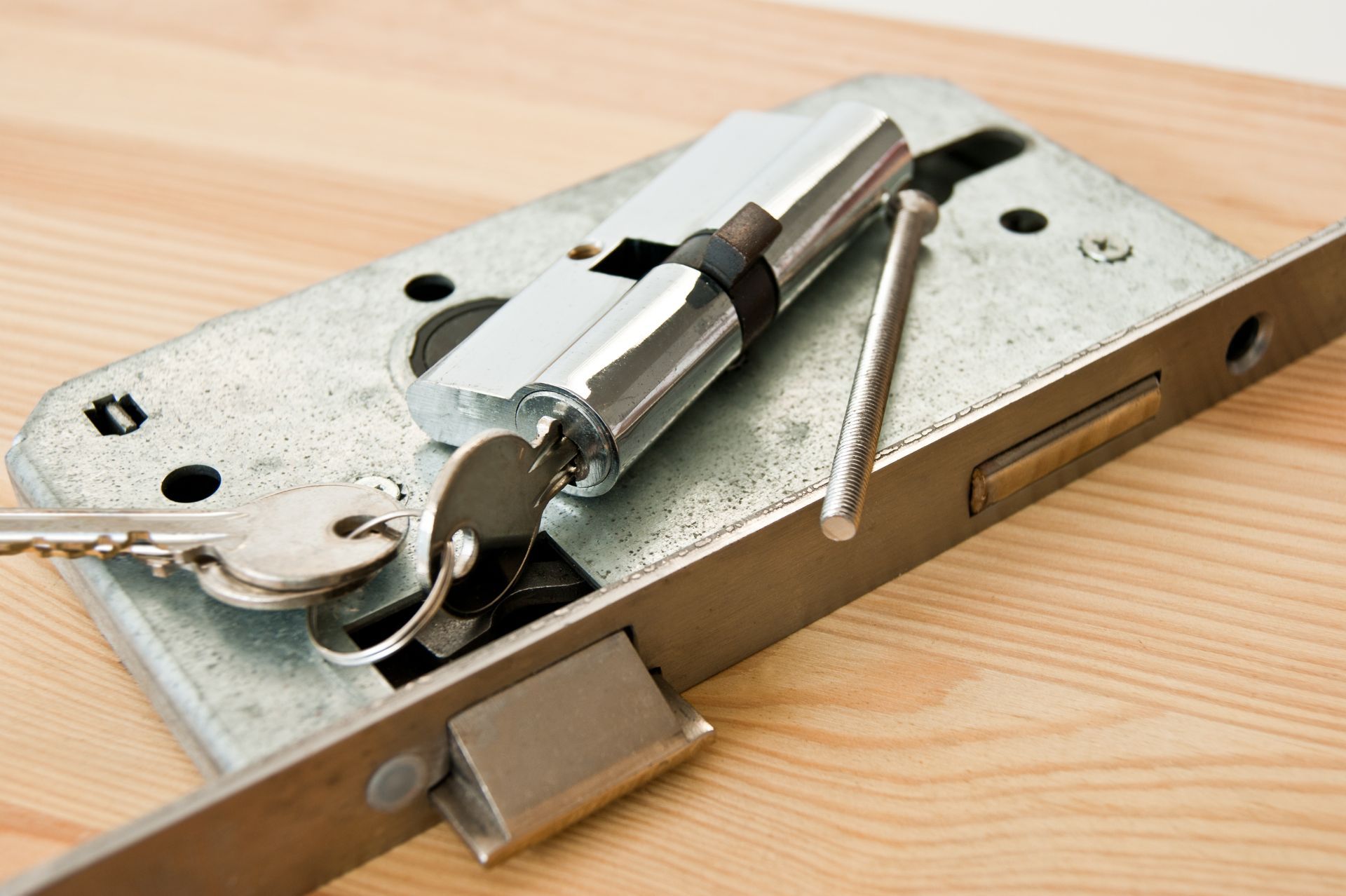 Un mécanisme de serrure de porte avec des clés posées sur du bois clair, laissant apparaître les pièces internes.