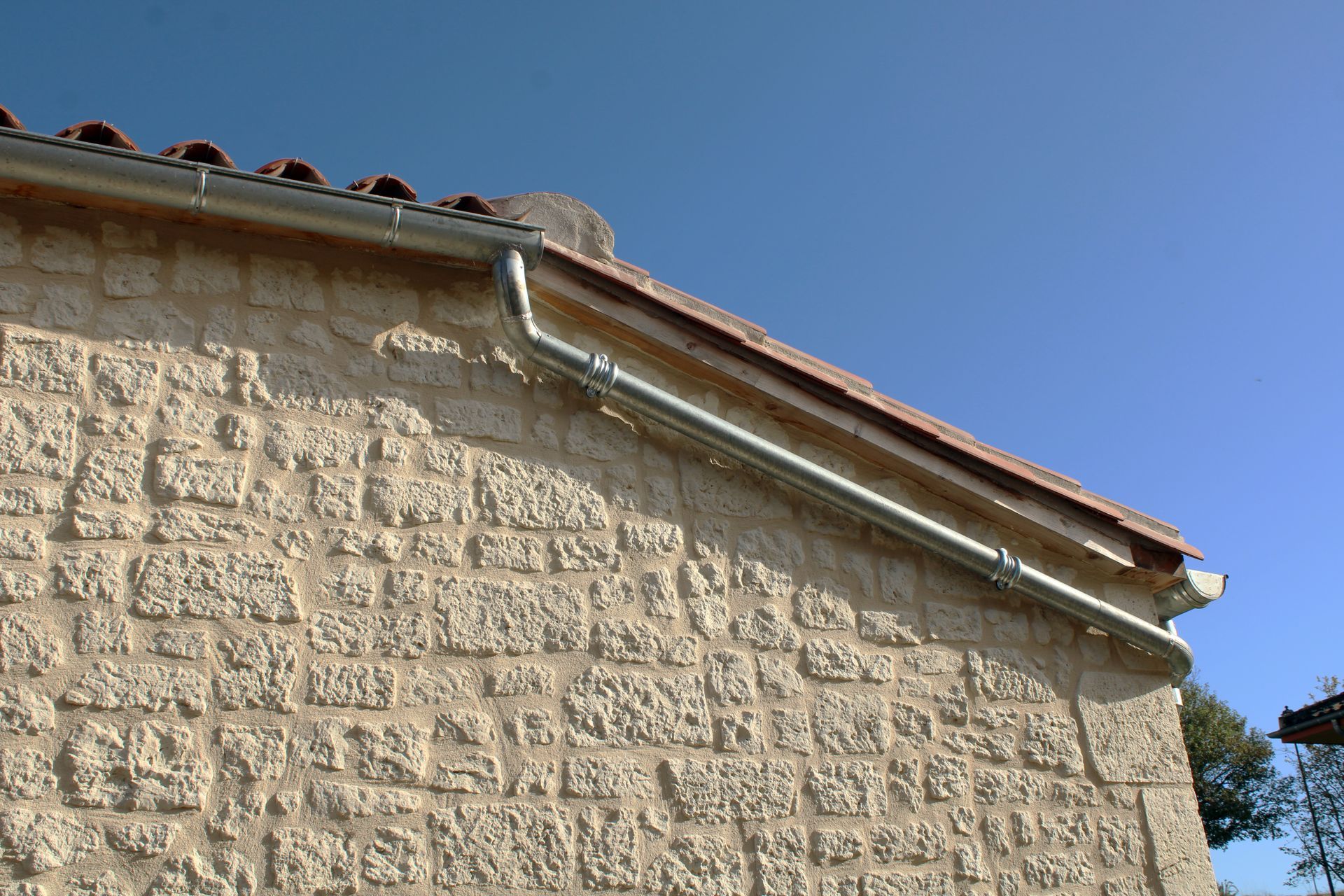 Gouttière en zinc gris sur la façade de la maison en pierre