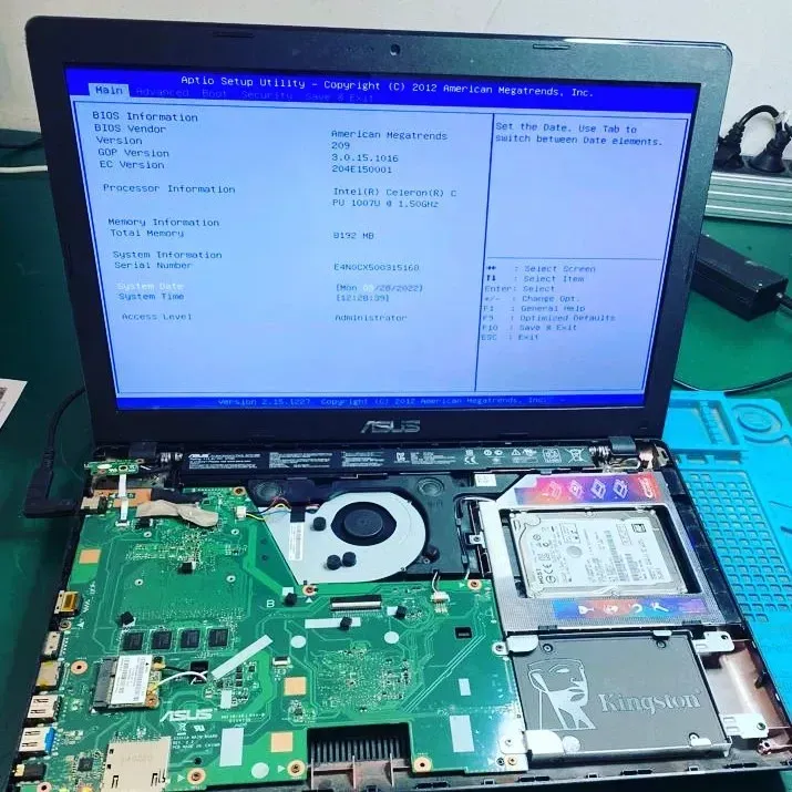 Portátil ASUS abierto con componentes internos y pantalla del BIOS expuestos sobre una mesa de trabajo.